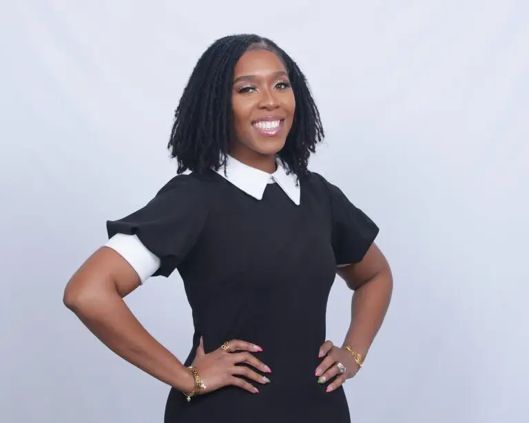 Anita Taylor standing with hands on her hips, exuding confidence in her black dress with a white collar.