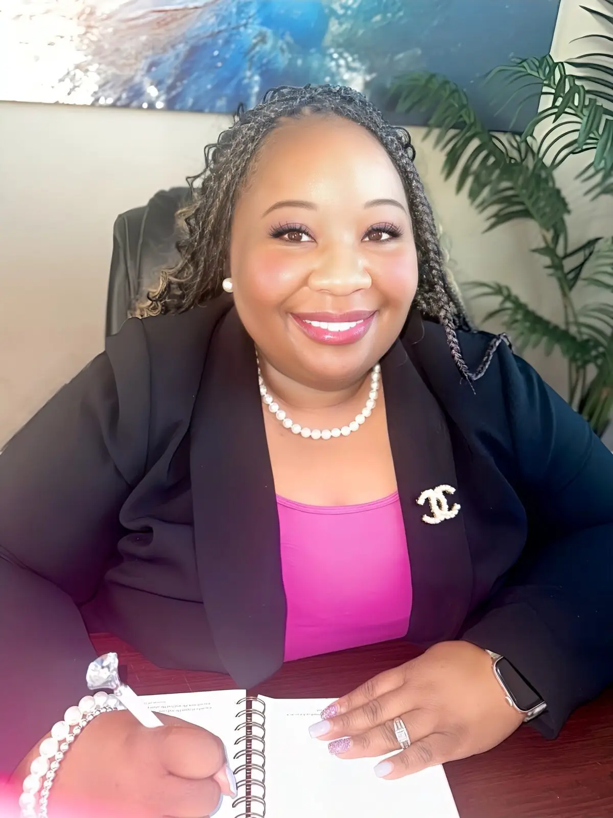 Erica Butler sitting at a desk, smiling confidently in a professional outfit with a stylish brooch and pearls, exuding warmth and professionalism.